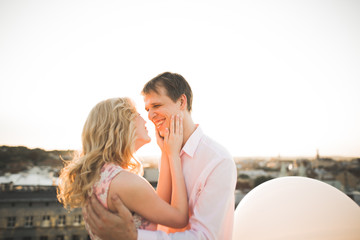Fototapeta premium Young couple in love posing on roof with perfect city view holding hands and hugging . Beautiful sunset