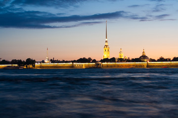 Fototapeta na wymiar Peter and Paul fortress with the Palace promenade at sunset on a background of pure pink sky with reflection in the water of the Neva river during the white nights in St. Petersburg