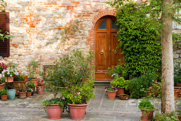 Fototapeta na wymiar Wooden door with flower pots in the medieval tuscan town Lucignano