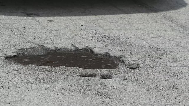 Tire Hits Pothole Puddle Slow Motion. a close up of a pothole filled with water. Truck tires hit it in slow motion splashing water everywhere
