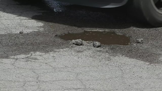 Tire Hits Puddle Pothole in Slow Motion Medium Shot. a close up of a pothole filled with water. Truck tires hit it in slow motion splashing water everywhere

