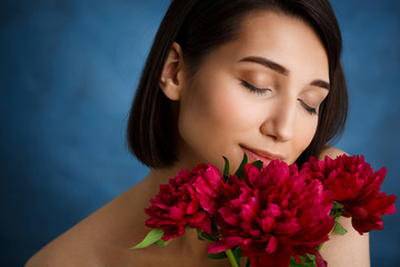 Naklejka premium Close up portrait of tender young girl with red flowers over blue background