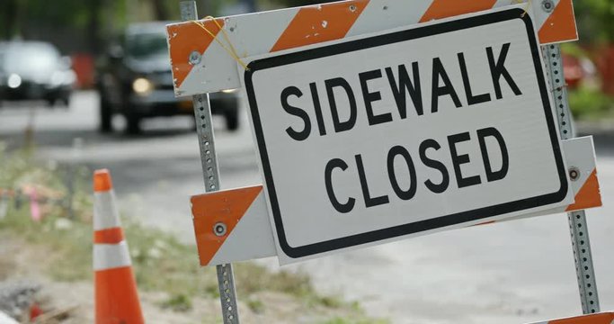 Sidewalk Closed Sign Close Up with Traffic. an angled shot of a sidewalk closed sign with traffic in the background

