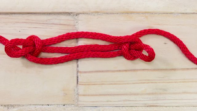 4k stop motion sheepshank knot made with red rope on wooden background.