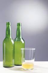 Two bottles and a glass of apple cider, over a grey background.