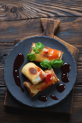 Basalt plate with crepes on a rustic wooden surface, top view
