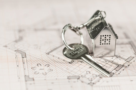 key with keychain in the form of a silver-colored house on a background of architectural drawing