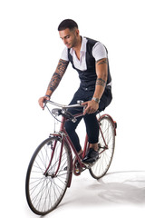 Portrait of young tattooed man in elegant clothes and shoes riding a bicycle.Isolate.Studio shot.