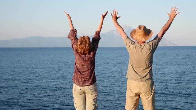 Woman and man with hands up standing on the top of the hill near the sea