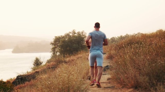 Man and woman jogging along a mountain path above a lake running away from the camera in an active lifestyle concept. Back view