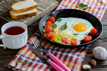 Fried eggs in pan with tomato, bread, pepper and parsley on wooden background