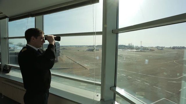 Air traffic controller is looking into distance in airport with binoculars