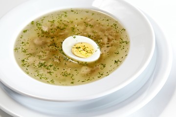 Low-fat chicken broth with a half cooked egg in a bowl isolated on white background