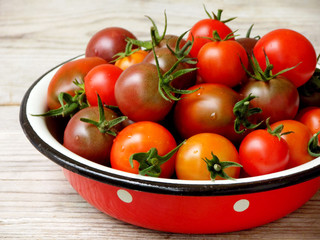 fresh red and black cherry tomatoes in a metal bowl on a wooden background. Side view