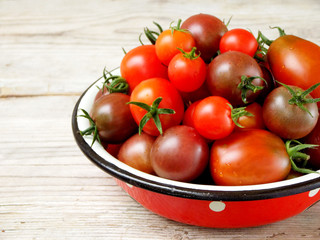 fresh red and black cherry tomatoes in a metal bowl on a wooden background. Side view