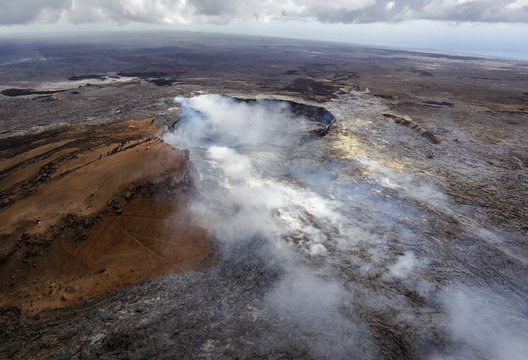 Smoking caldera of the Puu Oo vent with smaller crater in the foreground, Big Island, Hawaii. The lava field created by Puu Oo is in the background. Aerial photograph out of a helicopter.