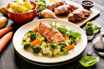 Baked chicken breast wrapped in bacon slices with boiled potatoes and steamed broccoli, carrot, garlic, onion