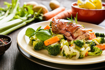 Baked chicken breast wrapped in bacon slices with boiled potatoes and steamed broccoli, carrot, garlic, onion