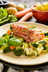 Baked chicken breast wrapped in bacon slices with boiled potatoes and steamed broccoli, carrot, garlic, onion