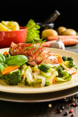 Baked chicken breast wrapped in bacon slices with boiled potatoes and steamed broccoli, carrot, garlic, onion