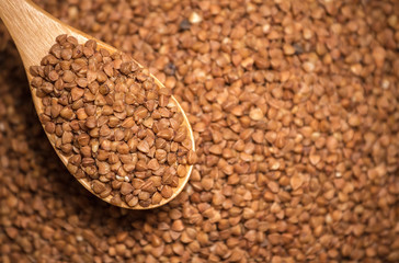 food background. Buckwheat in a wooden spoon, top view. Close-up