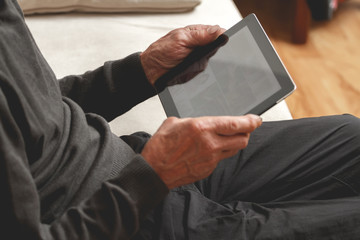 Senior sitting on the couch with a tablet in hands. Online education retirement concept. e-Learning. mock up