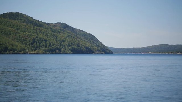 Steep bank of sea or lake with thick forest on a sunny day and blue sky.