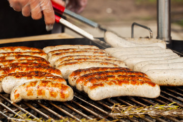 Hand with spatula flips sausages for hot dogs