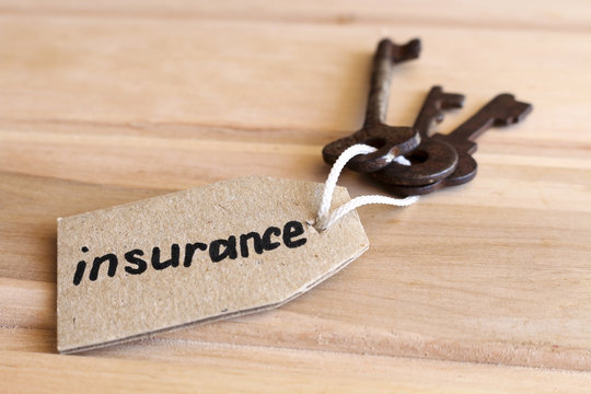 The concept of home insurance - the old key with the inscription on the tag on wooden background.