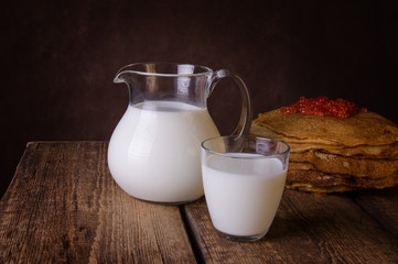 Glass jug and glass with milk on a wooden rustic background.