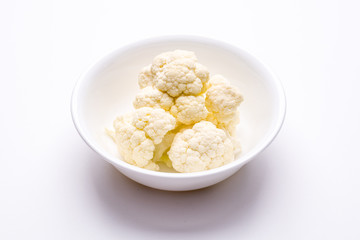 Fresh cauliflower in white bowl colander on a white surface.