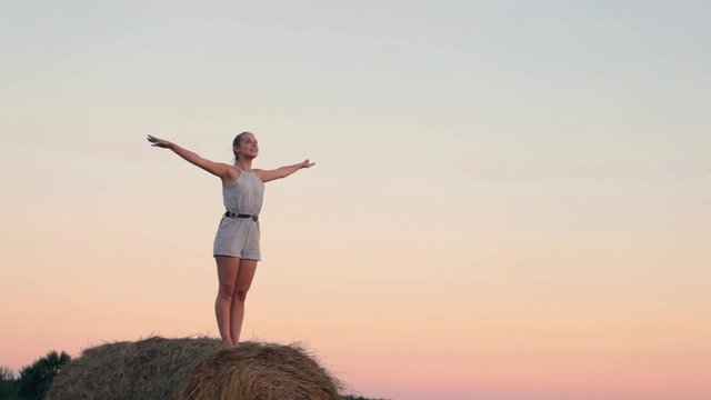 Beautiful young girl resting at stacks of hay at sunset