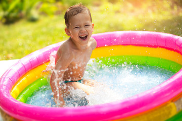 Little boy in inflatable swimming pool outdoor, having fun