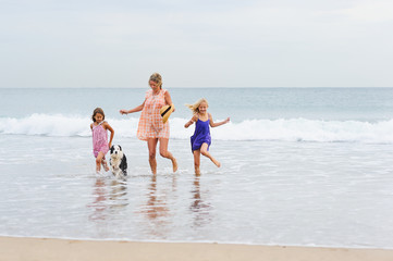 2 girls walking on beach with mom and dog. Happy family walking.