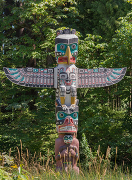 Vancouver, Canada - July 24, 2016: One of nine totem poles at Hallelujah point in Stanley Park. Detailed colors and features. Small wings. Dark colors fight with white hue. Green trees as background.