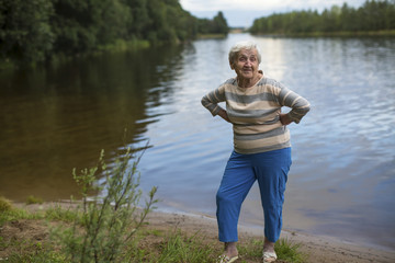 Fototapeta na wymiar An elderly woman stands on the shore of the lake.