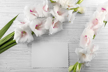 Beautiful gladiolus flowers with card on  wooden background