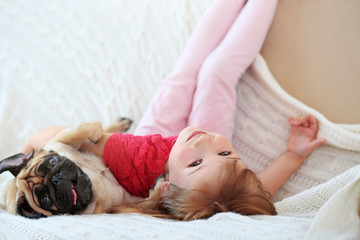 Adorable little girl and cute pug on couch