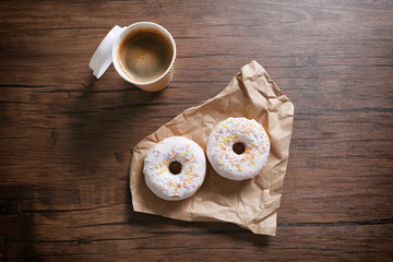 Paper cup of coffee and doughnuts on wooden background