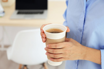 Female hands holding paper cup of coffee indoors