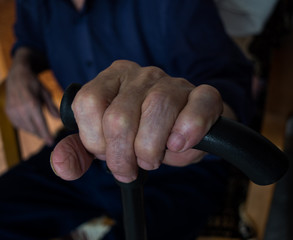 The old man's hand on a walking stick. Blurred silhouette of a man in the background.