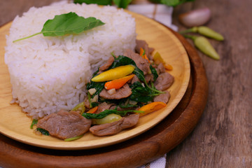 Stir fried spicy basil pork with white rice on wooden table, Thai food.