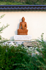 Buddha statue among the green branches in a garden of stones in the territory of a Buddhist temple. Datsan Rinpoche Bagsha on Bald Mountain in Ulan-Ude, Buryatia, Russia.