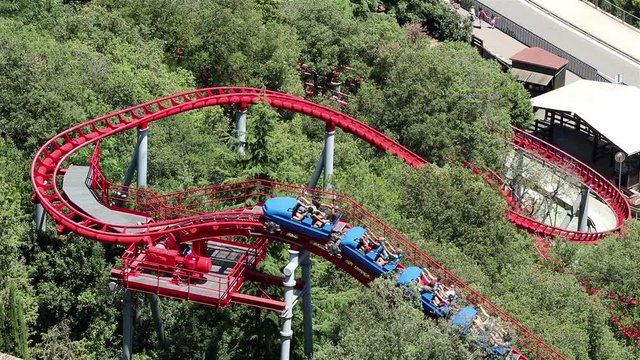 A blue rollercoaster climbing a red track in a green summer park, Tibidabo, Barcelona, Spain, July 2016