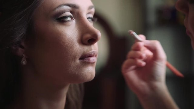 Closeup of a makeup artist applying makeup to a woman with perfect skin. Natural light from a window in front of a model.