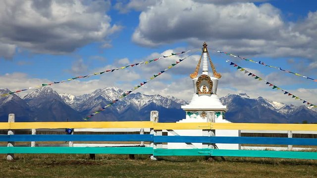 Buddhist stupa with colorful prayer flags in the background of mountains and blue sky with clouds