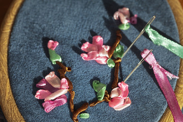 Needlework. Hand embroidery satin ribbons. Pink flowers and green leaves on a gray-blue suede