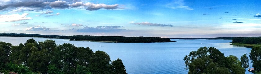 Fototapeta premium Piękna panorama nad brzegiem jeziora Jeziorak w Siemianach pojezierze iławskie, niebieska tafla wody oraz niebo z kilkoma chmurami