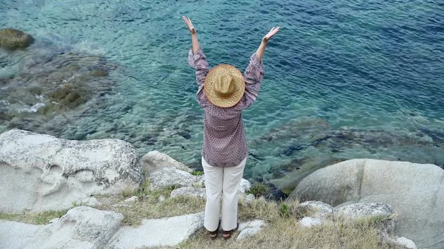 Woman with hands up standing on the hill near the sea