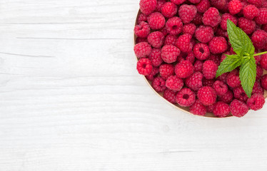 Plate of fresh raspberries with leaves of green mint on a white table, top view